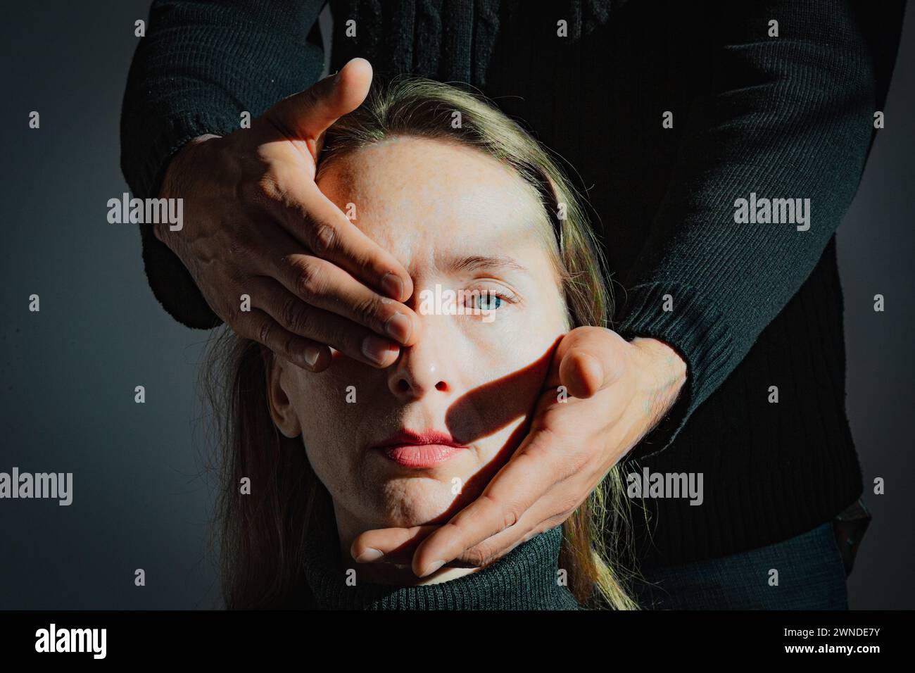 Visualizzazione di un problema psicologico. Difficoltà di comprensione reciproca. Un uomo tiene in mano la testa di una giovane donna adulta, chiudendo una Foto Stock