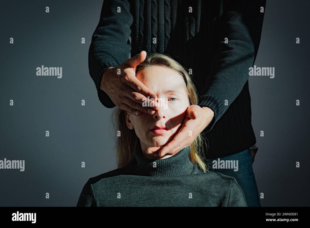 Visualizzazione di un problema psicologico. Difficoltà di comprensione reciproca. Un uomo tiene in mano la testa di una giovane donna adulta, chiudendo una Foto Stock
