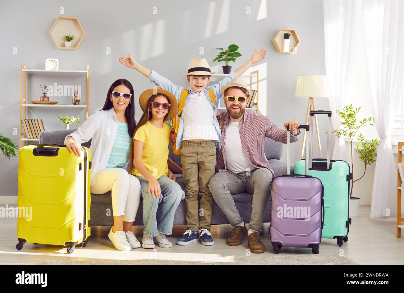 Famiglia felice con bambini seduti sul divano con valigie imballate pronte per le vacanze estive. Foto Stock
