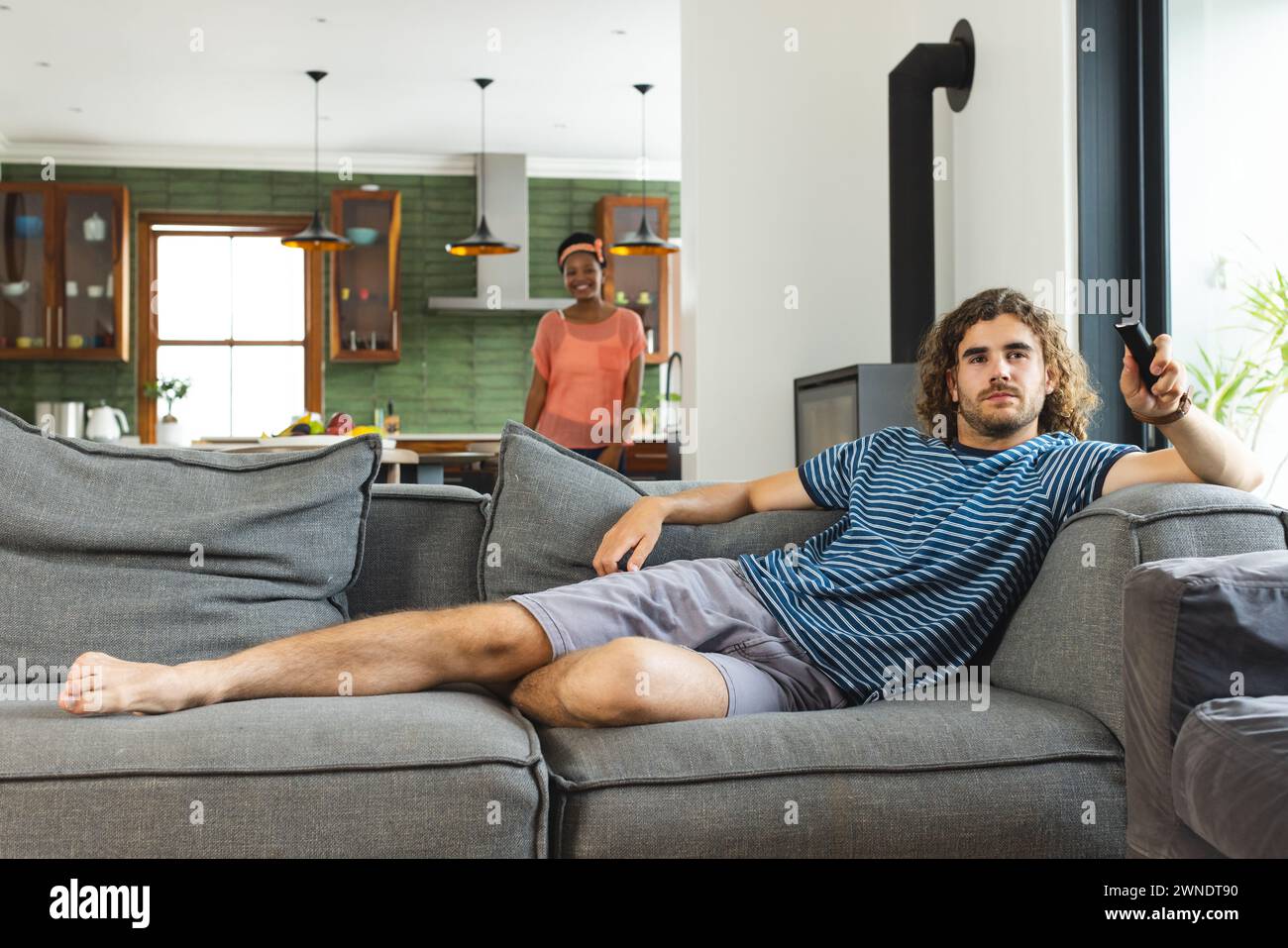 Diverse coppie di giovani uomini caucasici sdraiano su un divano grigio, tenendo un telecomando, con capelli ricci marroni Foto Stock