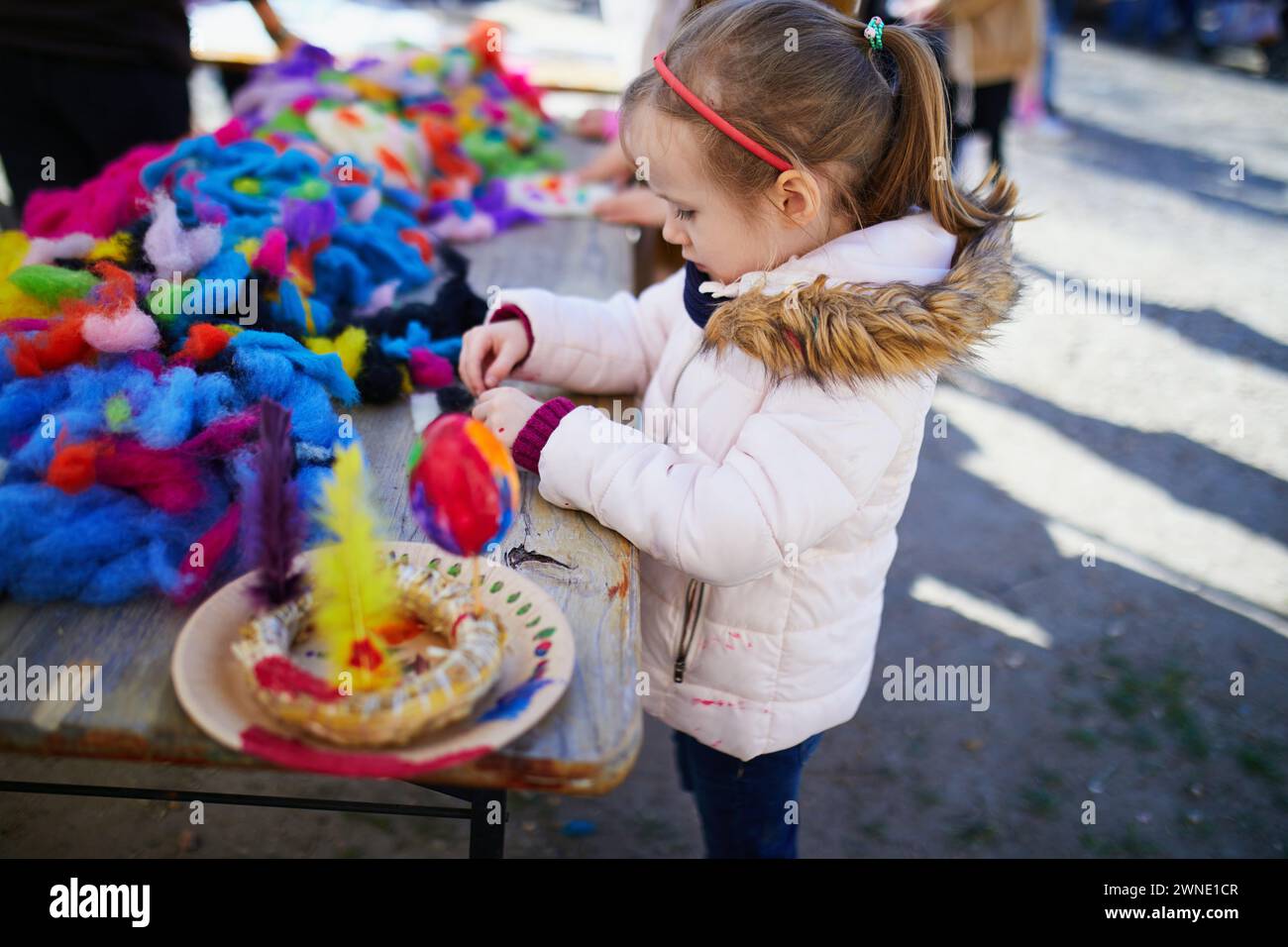 Adorabile bambina in età prescolare che realizza attività artigianali fai-da-te per la Pasqua all'aperto. I bambini dipingono uova colorate per la caccia pasquale. Il bambino si prepara per la festa di Pasqua. Fa Foto Stock