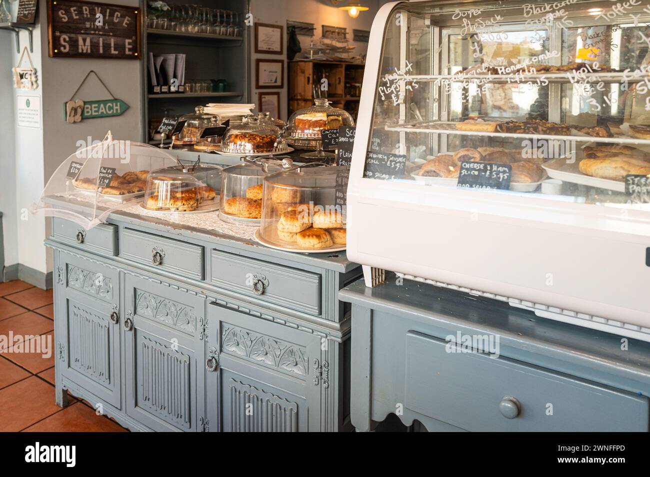 Il bancone di una caffetteria cittadina di mare mostra una selezione di torte e dolciumi sotto vetri. Foto Stock