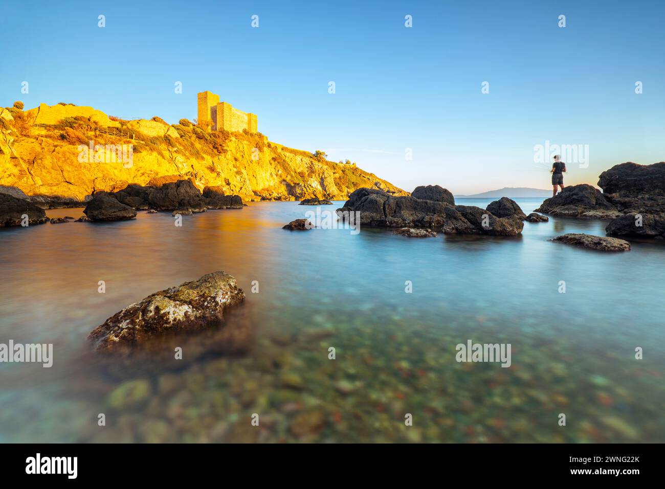 Il castello di Rocca Aldobrandesca sulla costa rocciosa della Maremma a Talamone nel tramonto dorato, Toscana, Italia Foto Stock