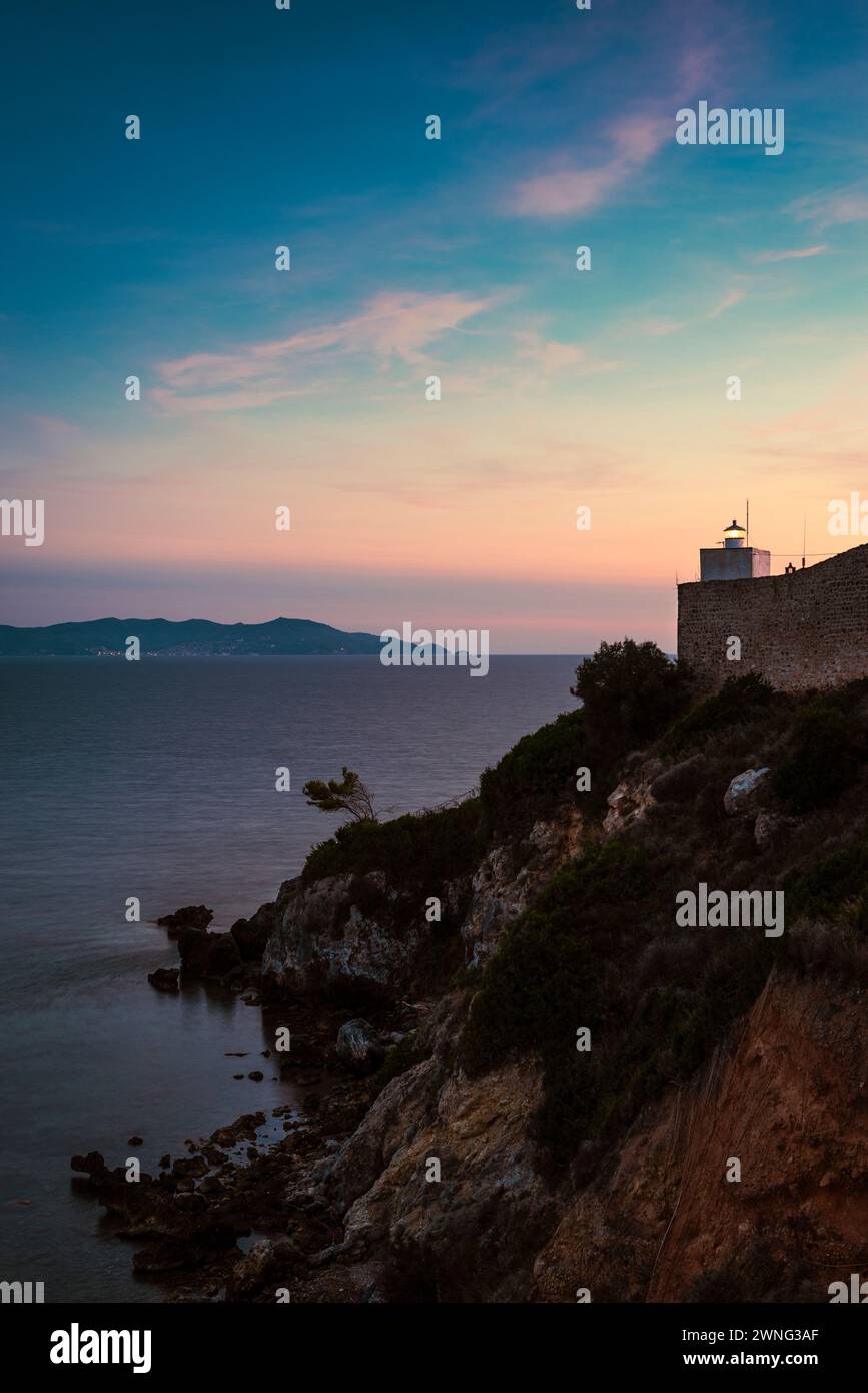Faro di Talamone di fronte al mare e Monte Argentario al crepuscolo, Toscana, Italia Foto Stock