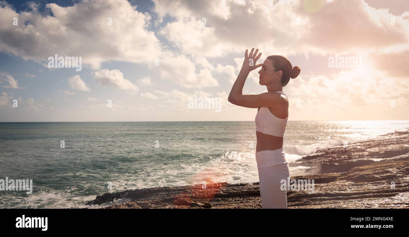 donna in piedi sulle rocce in riva al mare che meditava e praticava yoga, bagliore del sole. Foto Stock