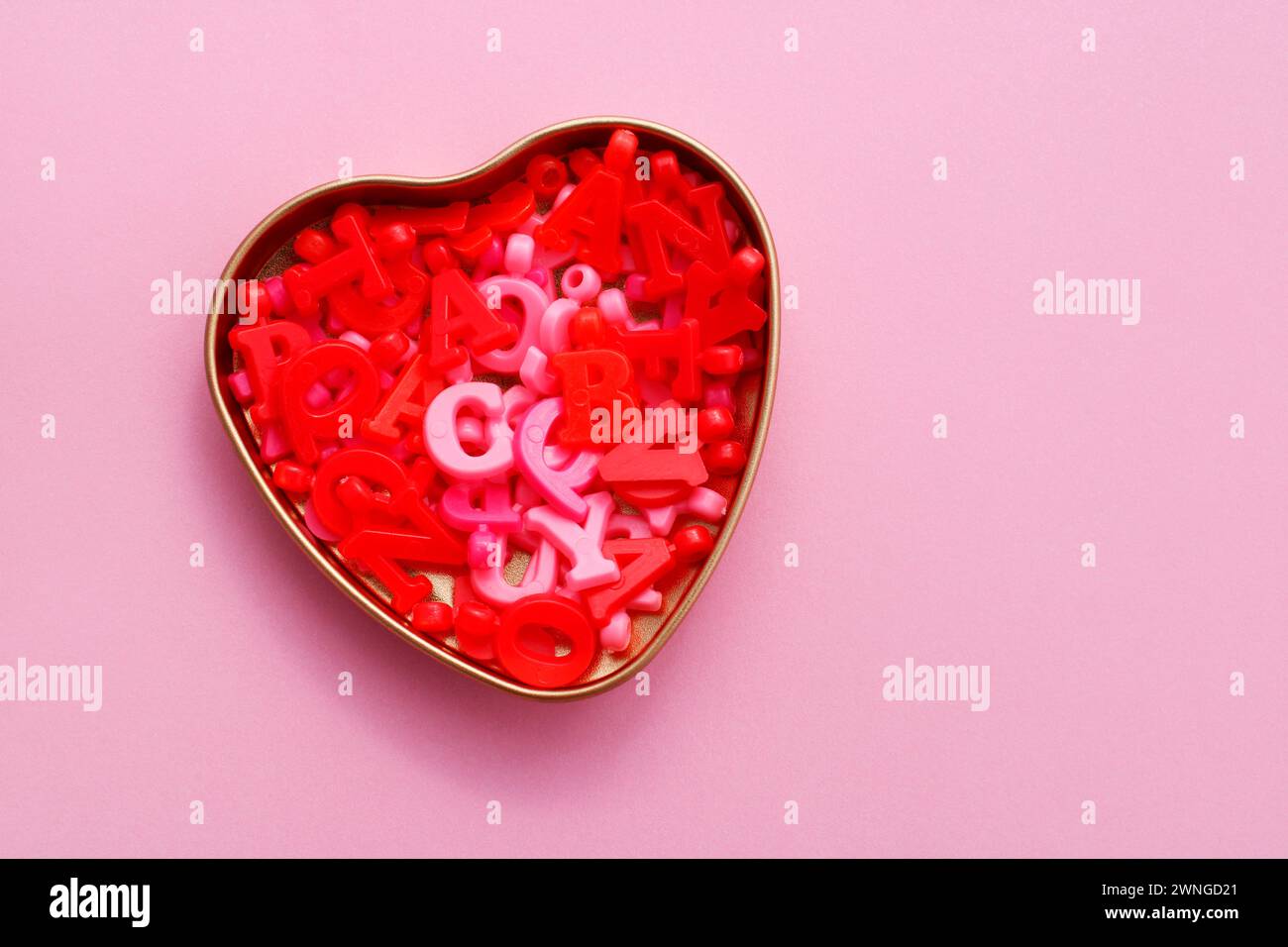Contenitore a forma di cuore contenente perline a forma di lettera rosa e rossa Foto Stock