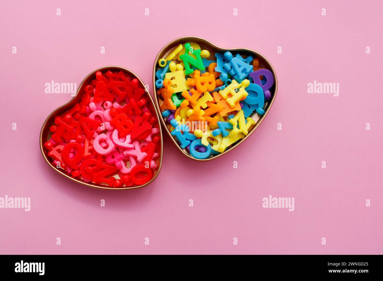 Due contenitori a forma di cuore contenenti perline colorate a forma di lettera Foto Stock