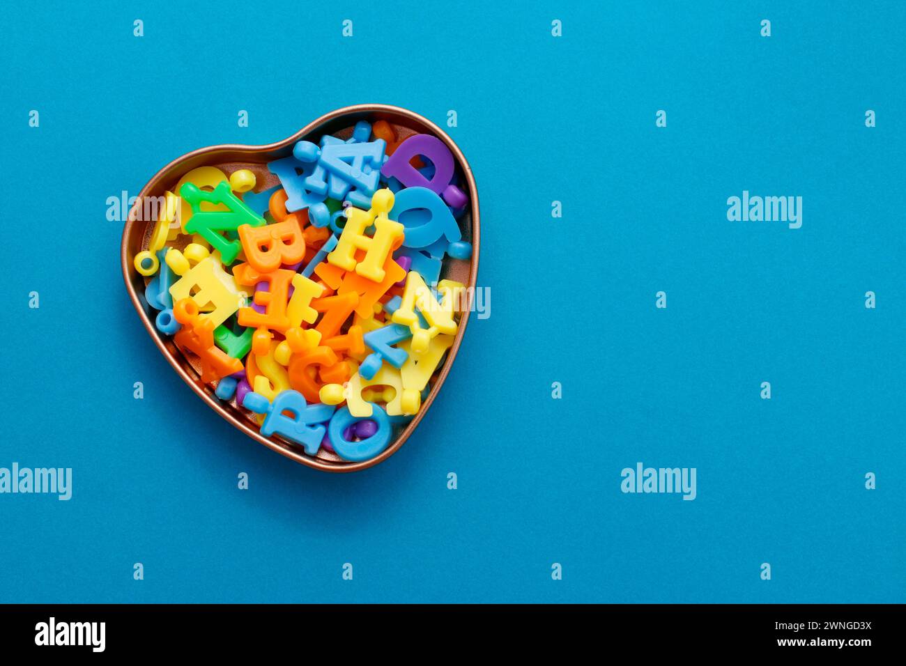 Contenitore a forma di cuore contenente perline colorate a forma di lettera Foto Stock
