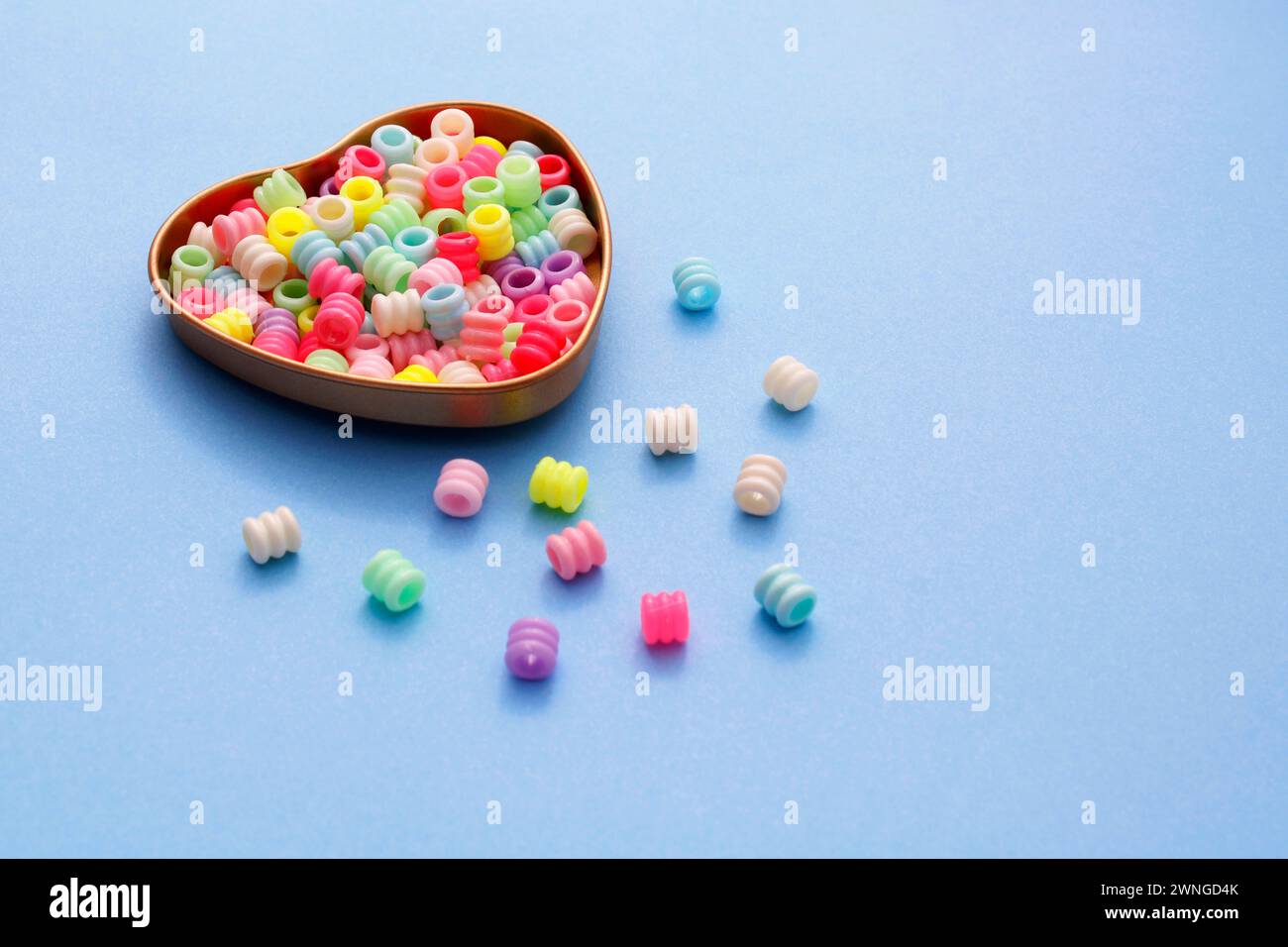 Contenitore a forma di cuore contenente perle cilindriche di plastica colorate Foto Stock