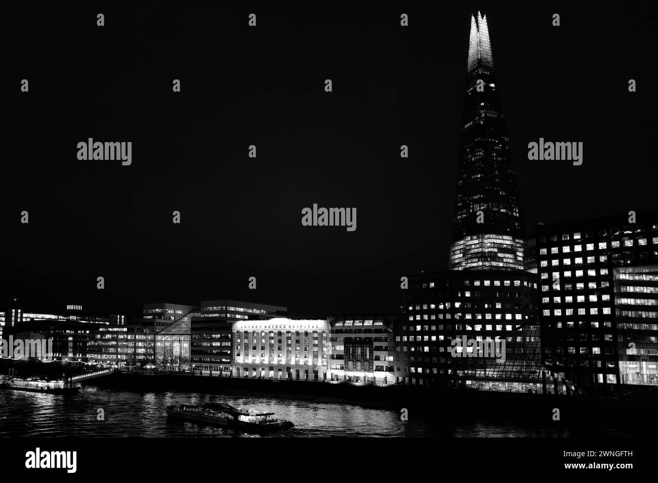 Potente paesaggio notturno astratto monocromatico illuminato architettonico dello Shard e del Tamigi girato dal London Bridge e mostra Tooley Street, London Bridge Hospital, HMS Belfast, London Bridge City Pier e River Boats Foto Stock