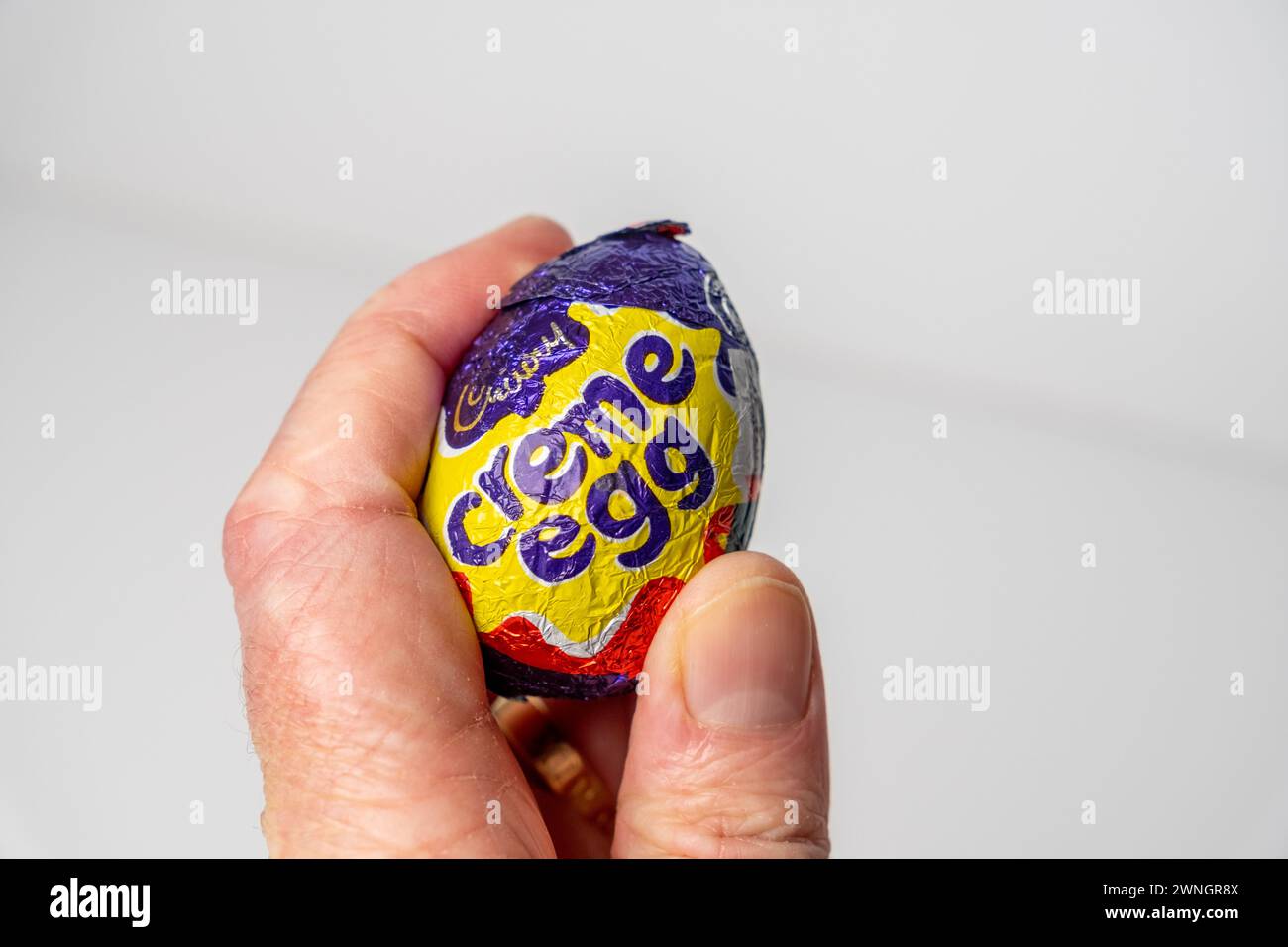 Norwich, Norfolk, Regno Unito – 02 marzo 2024. Primo piano di una mano umana non identificabile che tiene un uovo di Cadbury Creme Foto Stock