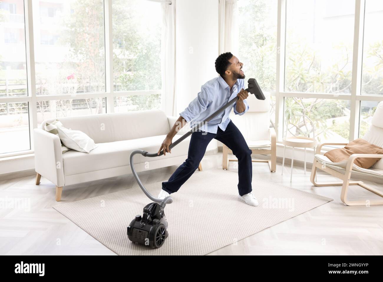 Eccitato, giovane e divertente proprietario africano che canta a hoover Foto Stock