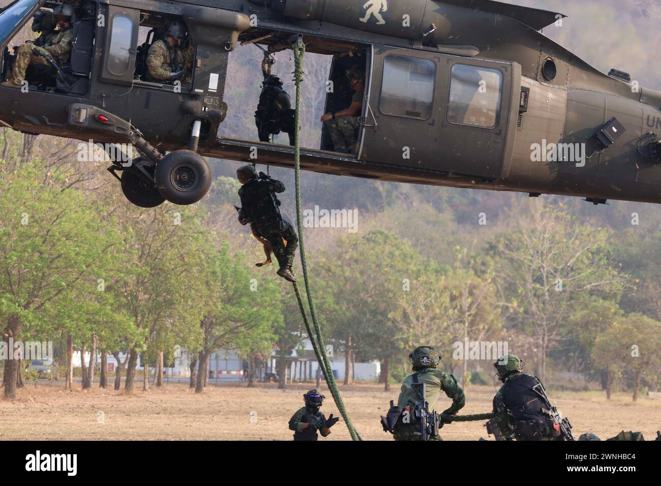 Soldati dell'esercito reale thailandese con il Royal Thai Army Special Warfare Command, corda veloce fuori da un UH-60 Blackhawk dell'esercito statunitense assegnato al 2-158th Assault Helicopter Battalion, 16th Combat Aviation Brigade, 7th Infantry Division, durante l'addestramento del sistema veloce di inserimento ed estrazione della corda (PATATINE FRITTE), Lop Buri, Thailandia, 28 febbraio 2024, durante l'esercizio congiunto annuale Cobra Gold 2024. L'esercizio congiunto Cobra Gold è un esempio positivo di cooperazione multilaterale e si trova in netto contrasto con altri esempi della regione, che sfidano l'ordine internazionale basato su regole attraverso una sicurezza espansiva e assertiva A. Foto Stock