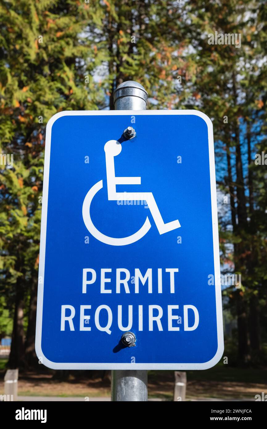 Segnaletica di parcheggio per disabili con sfondo alberato. Parcheggio per disabili. Cartello blu per disabili. Cartello di permesso parcheggio disabilitato sul palo. Parcheggio riservato l Foto Stock
