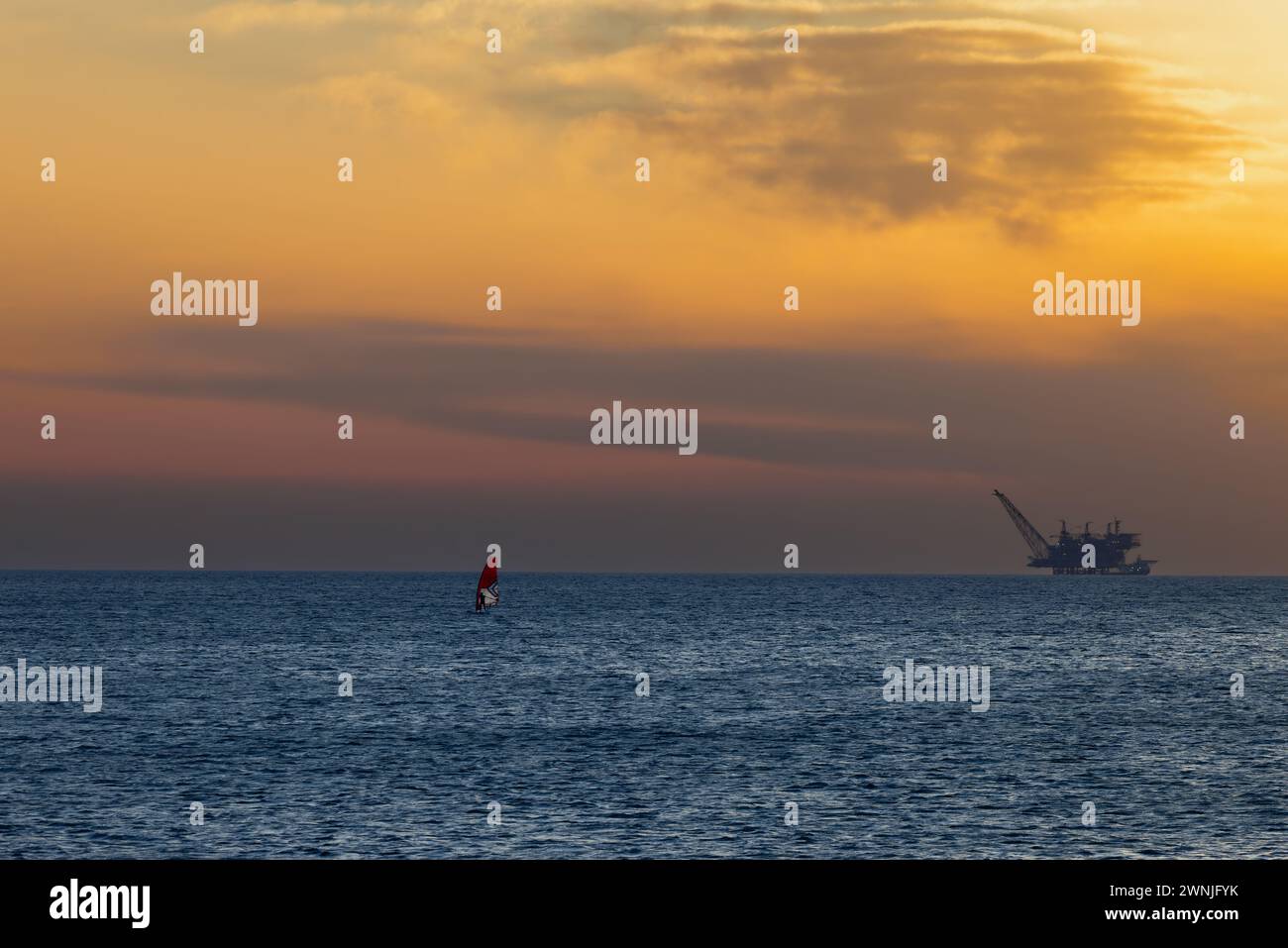 Sali a bordo con la vela e la piattaforma a gas in mare al tramonto a Nachsholim in Israele Foto Stock