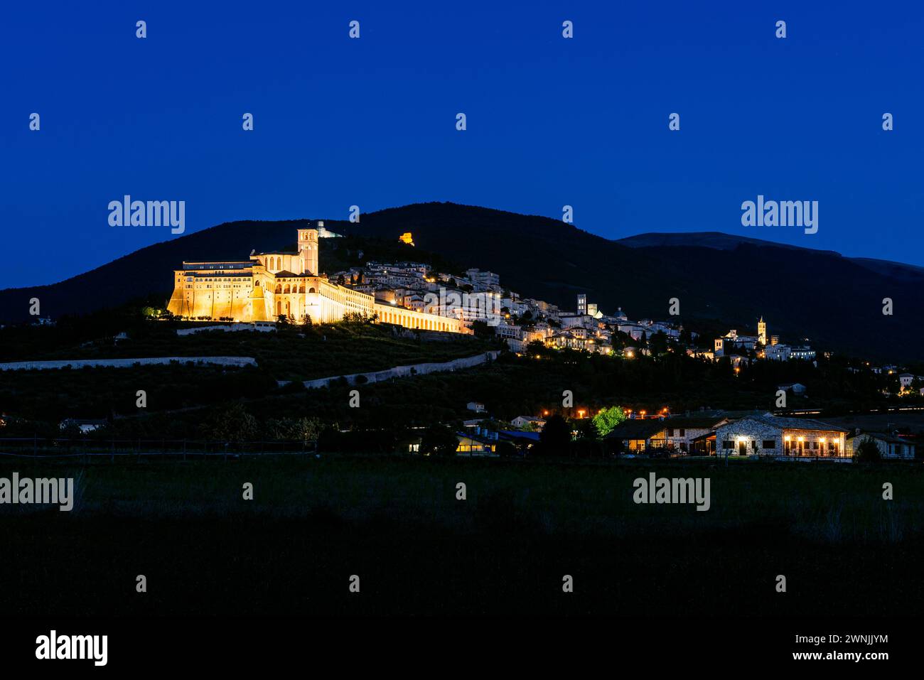 Vista della città vecchia illuminata di Assisi con il monastero e la basilica di San Francesco e Santa chiara di notte, Umbria, Italia Foto Stock