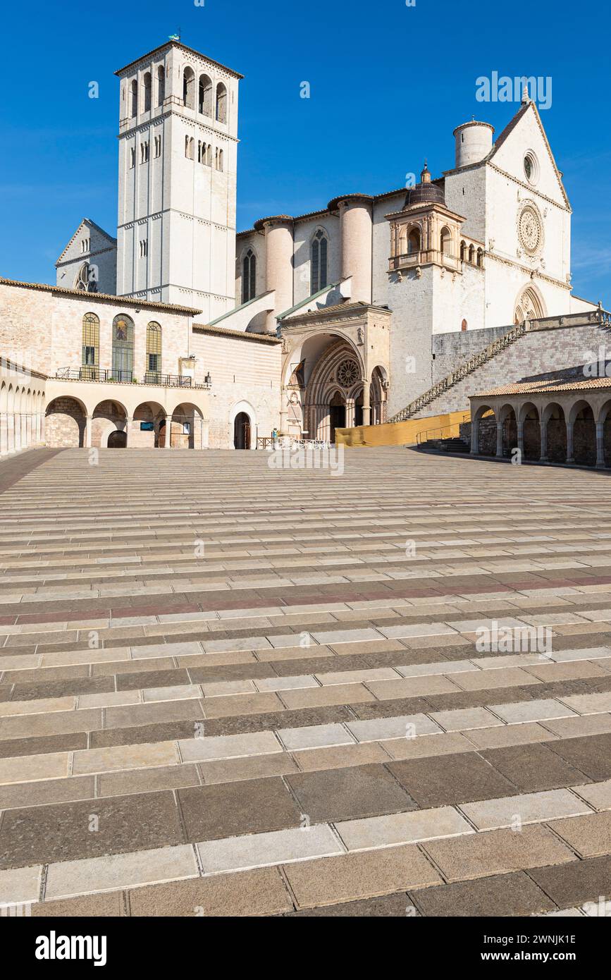 I colonnati circondano la piazza inferiore di fronte alla Basilica di San Francesco d'Assisi al sole del mattino, Umbria, Italia Foto Stock