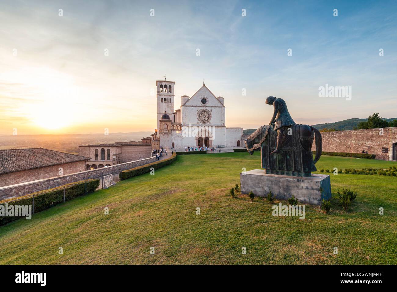 Die Basilika des HL. Franziskus von Assisi mit einer bronzenen Reiterstatue im Sonnenuntergang, Umbrien, Italien Foto Stock