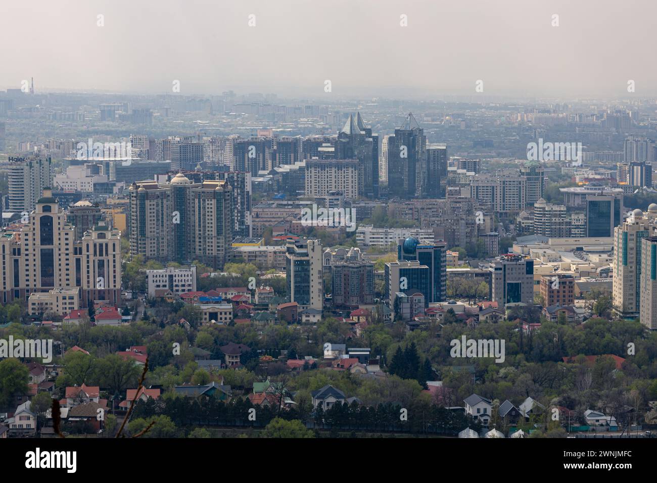 Combinazione di basso e alto sviluppo urbano. Vista panoramica su Almaty dal parco del monte Kok Tobe. Paesaggio urbano in primavera. Fumi di foschia al di sopra di t Foto Stock