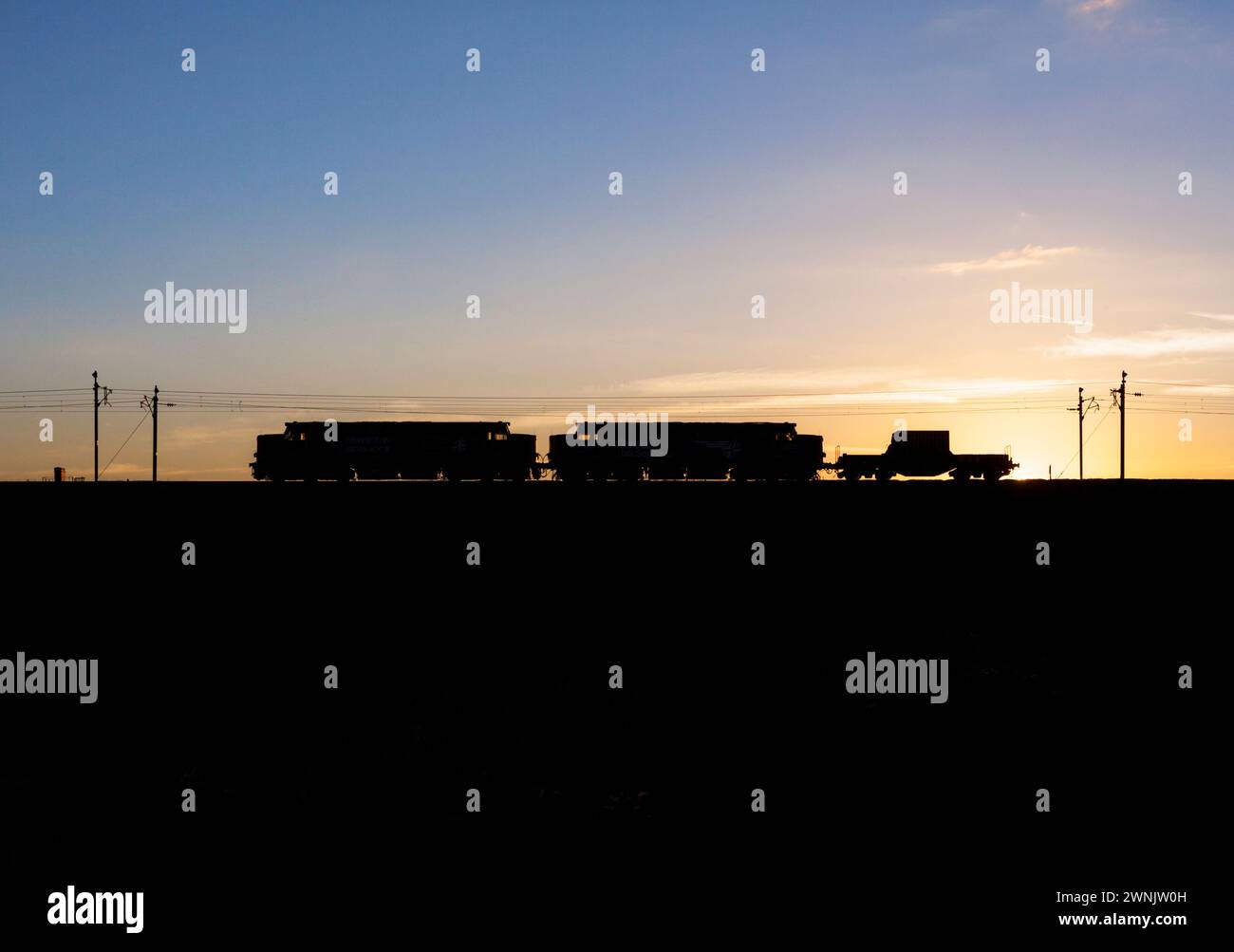 Una sagoma di 2 locomotive diesel di classe elettrica inglese 37 che trasportano matracci nucleari sulla linea principale della costa occidentale al tramonto Foto Stock