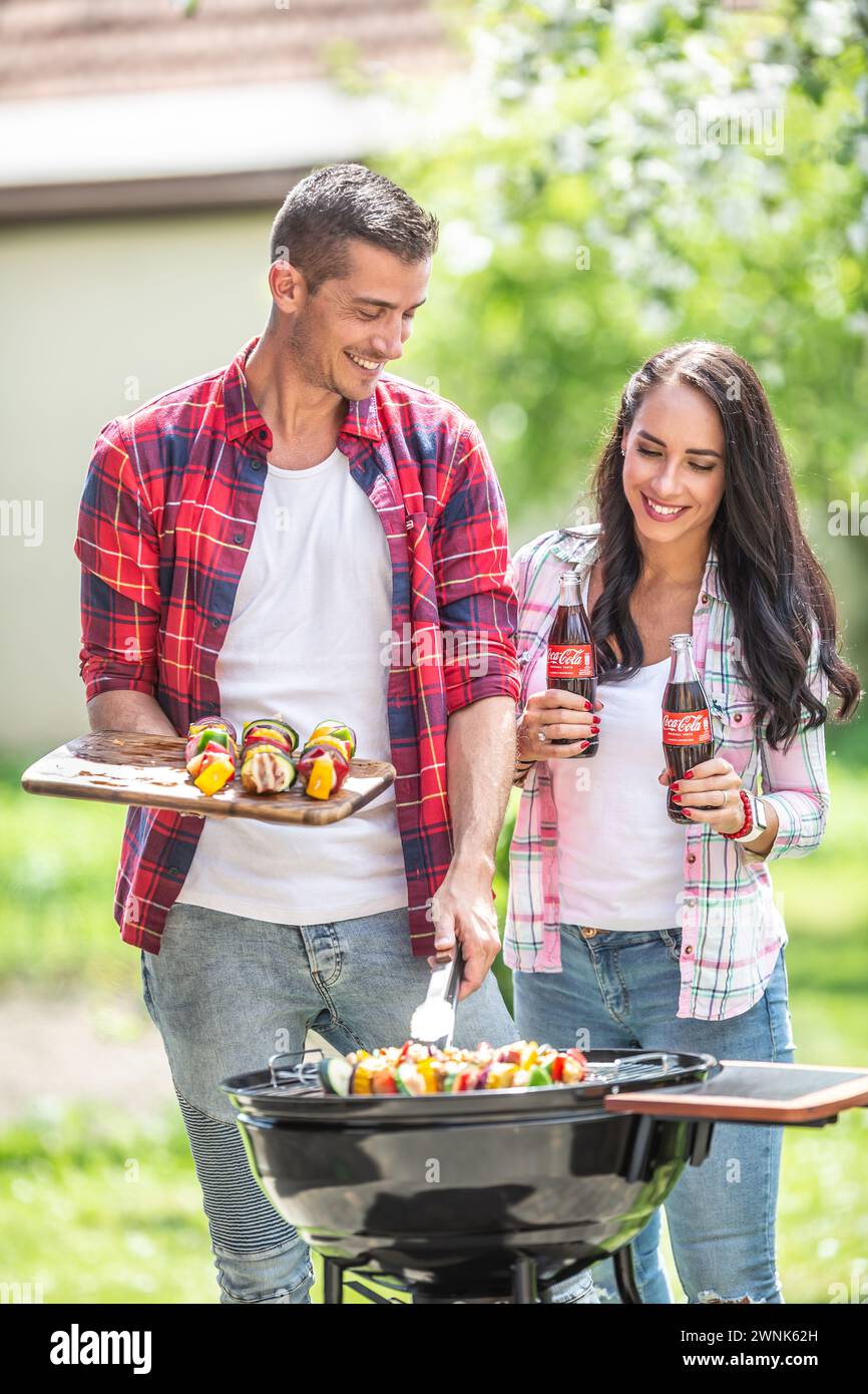 Marzo. 02. 2024 Liptovsky Mikulas. Slovacchia - amici di sesso maschile e femminile condividono la festa estiva al barbecue con carne e verdure alla griglia e bottiglie di coca Foto Stock