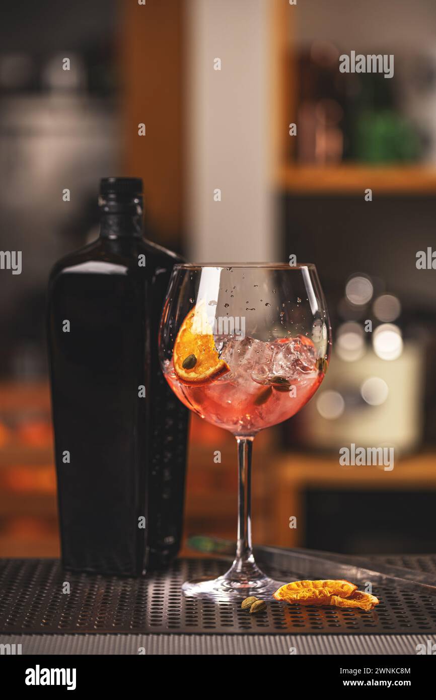 Cocktail di gin rosa servito in un bicchiere di palloncino con cubetto di ghiaccio e fetta di arancia Foto Stock