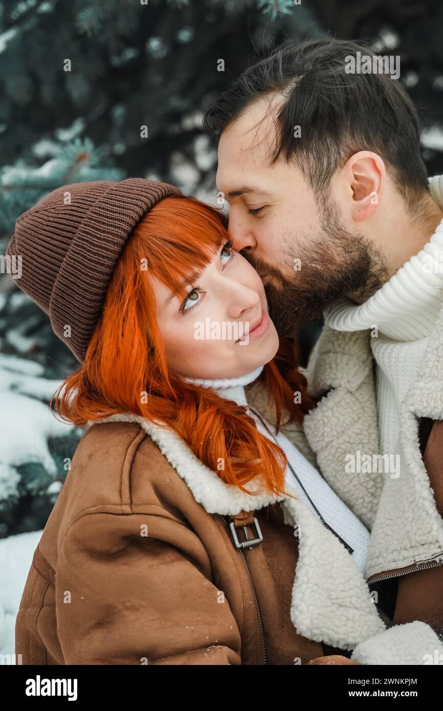 Amore romantico soggiorno di coppia. Brutale uomo barbuto, brillante ragazza dai capelli rossi nel parco invernale. Appuntamento romantico, baci, abbracci. Camminare, divertirsi. Foto Stock