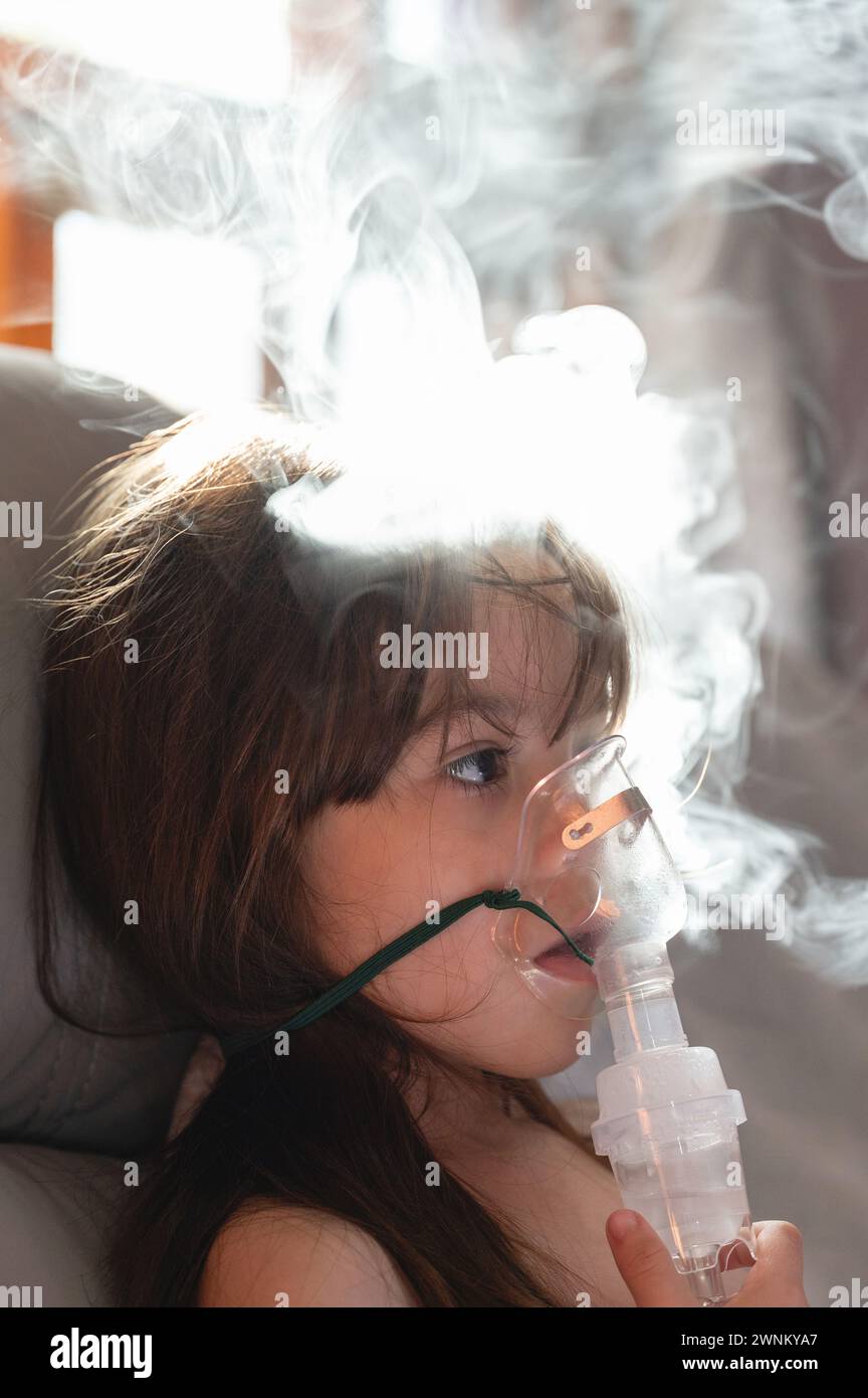 Calmare la bambina usando la maschera del nebulizzatore con sfondo fumoso Foto Stock