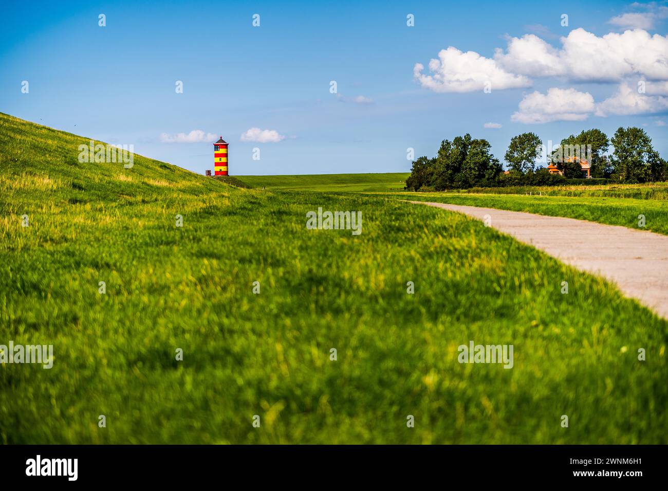 Un faro colorato sorge su una collina verde sotto un cielo blu con nuvole, il faro di Pilsum, Greetsiel, Norden, Frisia orientale, bassa Sassonia Foto Stock