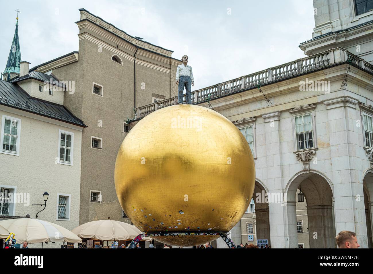 Uomo in piedi su una grande scultura di palla d'oro in una piazza affollata alla luce del giorno, Salisburgo, Austria Foto Stock