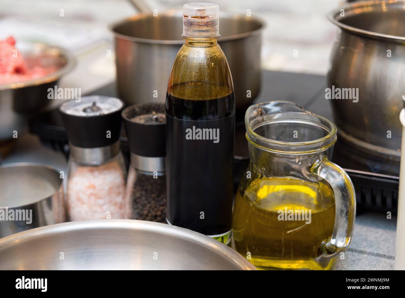Una preparazione culinaria con olio d'oliva in una caraffa di vetro trasparente, aceto in bottiglia e macinacaffè per sale e pepe, pronti per l'insaporire. Foto Stock
