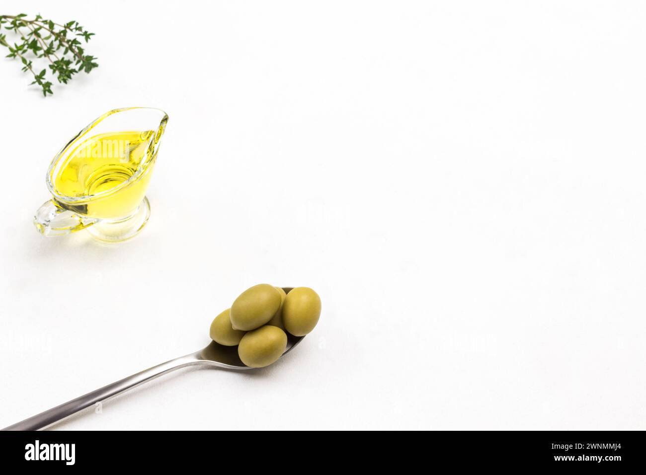 Olive verdi in cucchiaio di metallo. Olio d'oliva in vaso di vetro. Ciuffi di timo. Copia spazio. Sfondo bianco. Vista dall'alto. Foto Stock