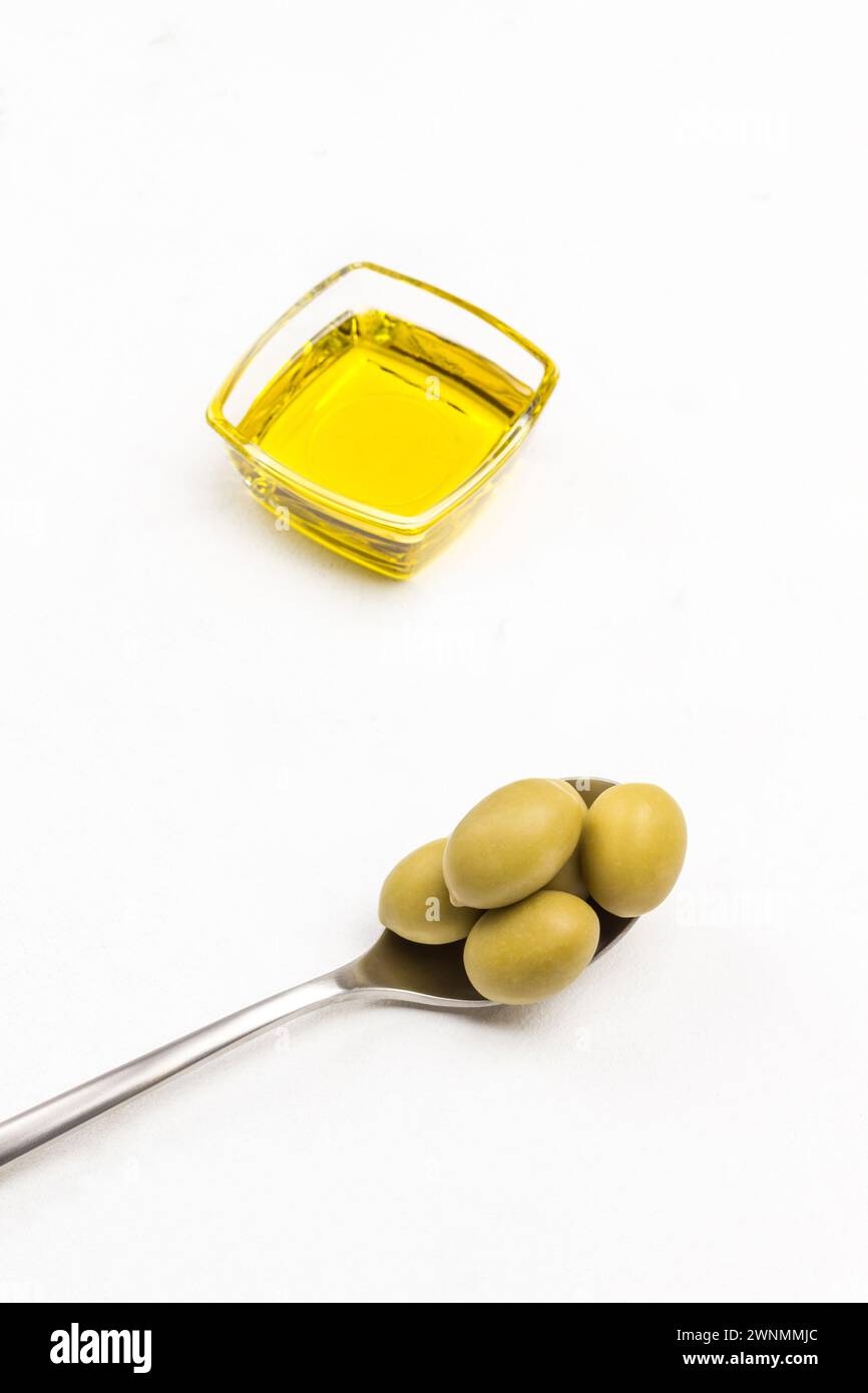 Olive verdi in cucchiaio di metallo. Olio d'oliva in vaso di vetro. Ciuffi di timo. Sfondo bianco. Vista dall'alto. Foto Stock