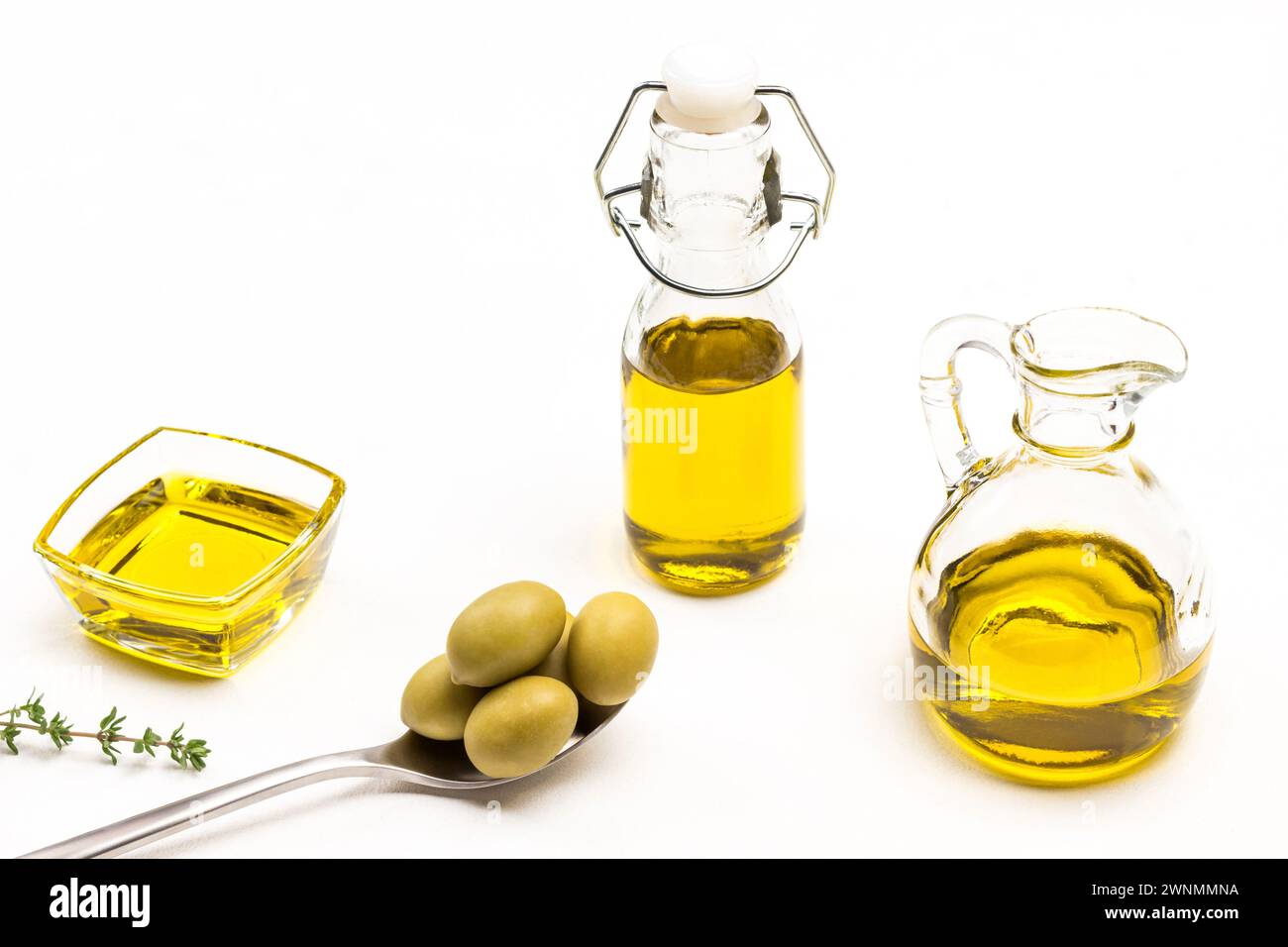 Olive verdi in cucchiaio di metallo. Olio d'oliva in vaso di vetro. Ciuffi di timo. Sfondo bianco. Vista dall'alto. Foto Stock