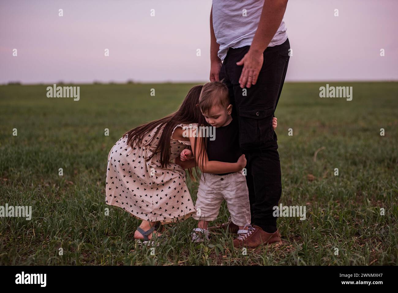 Il giovane padre corre con il figlio piccolo in braccio e la figlia maggiore attraverso il campo verde. Diversita' tempo giocoso in famiglia a Meadow. Festa dei padri. Foto Stock