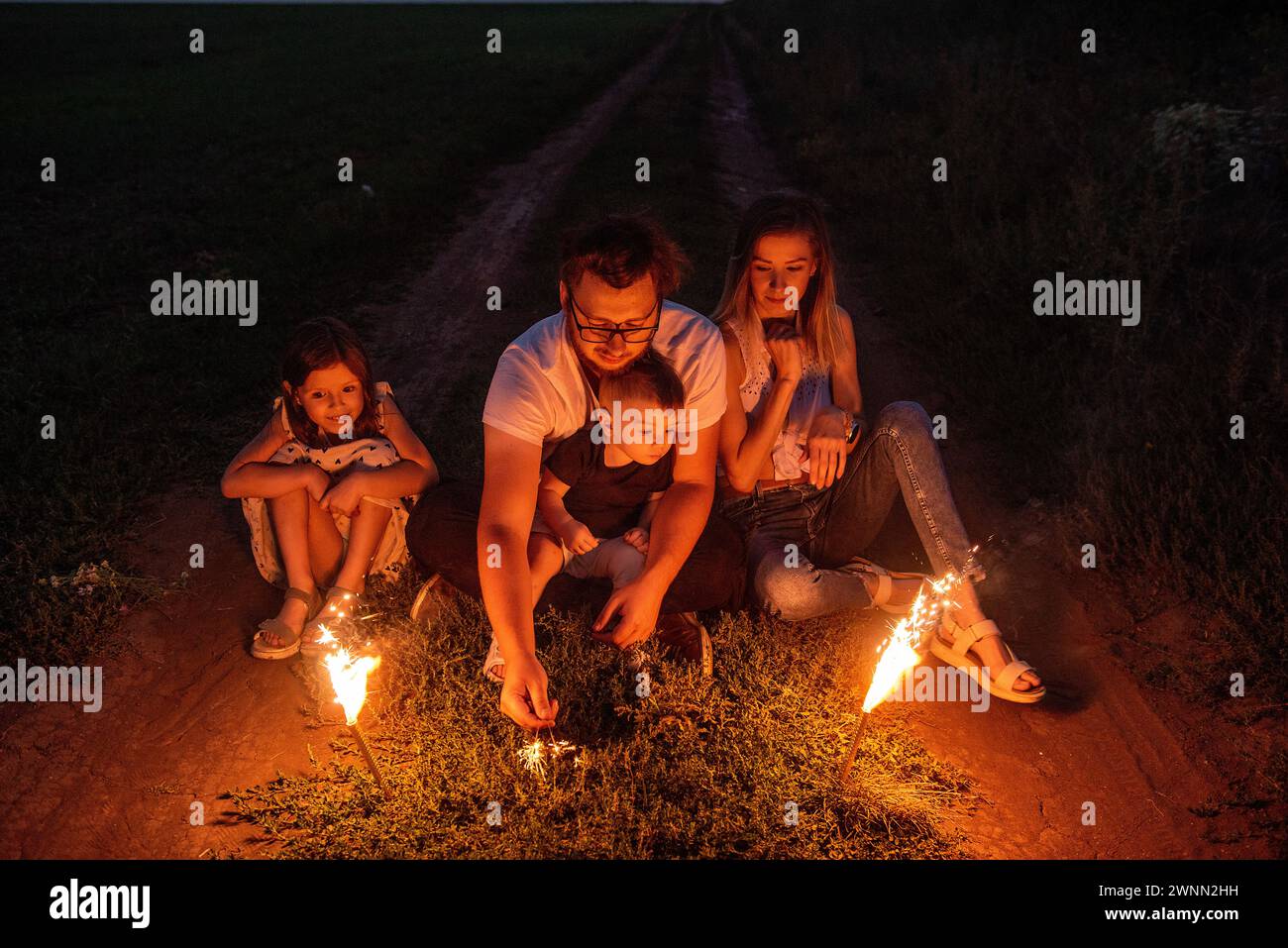 Nell'incantevole notte, una famiglia accende scintillanti su un sentiero remoto, crogiolandosi nella calda luce festosa, creando ricordi duraturi insieme. Diversi Foto Stock