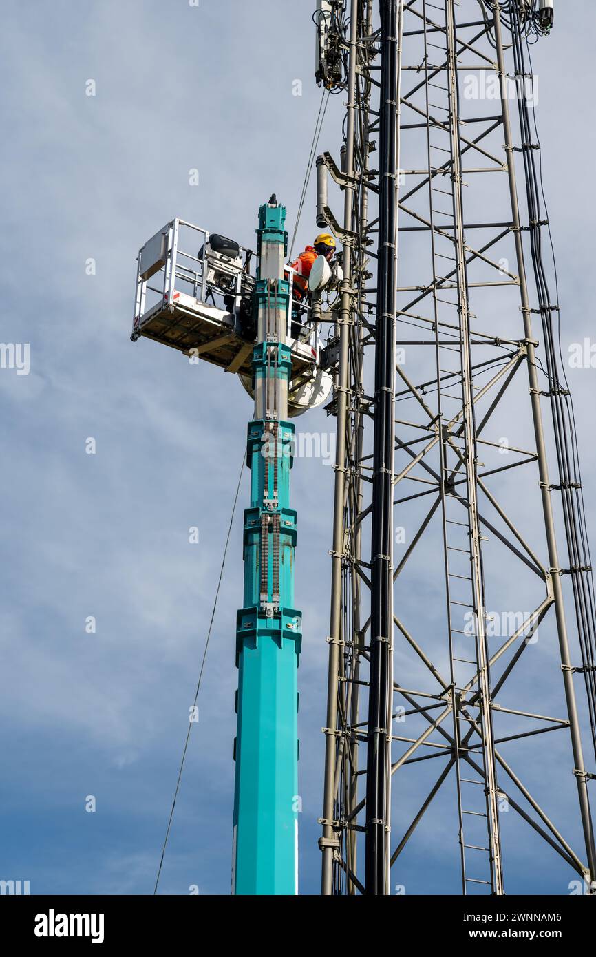 I tecnici su una piattaforma gru eseguono la manutenzione su una torre per telecomunicazioni Foto Stock