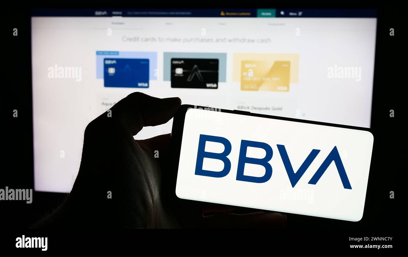 Persona che detiene un telefono cellulare con il logo della società Banco Bilbao Vizcaya Argentaria SA (BBVA) di fronte alla pagina web aziendale. Mettere a fuoco il display del telefono. Foto Stock