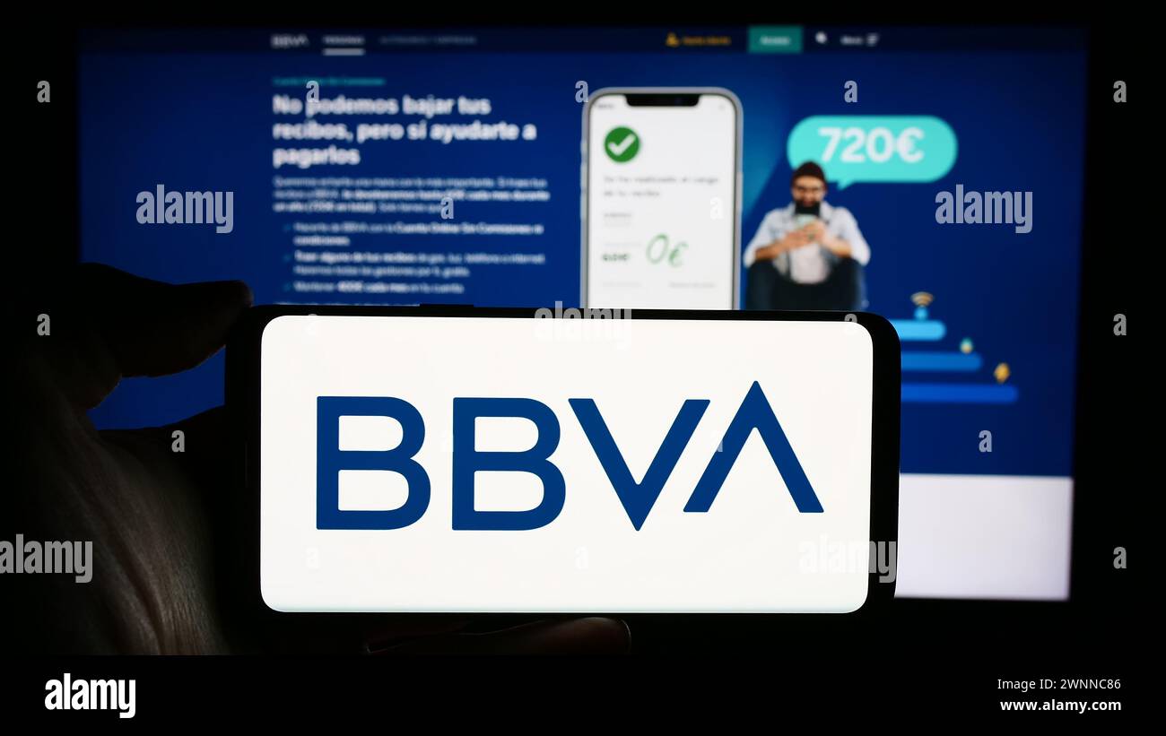 Persona che detiene un cellulare con il logo della società Banco Bilbao Vizcaya Argentaria SA (BBVA) di fronte alla pagina web aziendale. Mettere a fuoco il display del telefono. Foto Stock