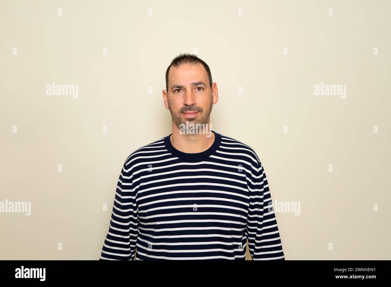 Uomo ispanico con barba che indossa un maglione a righe che sorride sullo sfondo beige dello studio. Foto Stock