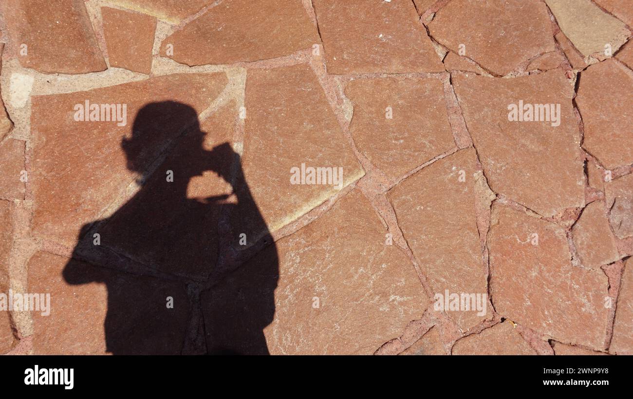 Una foto creativa e artistica di un'ombra che regge una fotocamera proiettata su una superficie in pietra. Foto Stock
