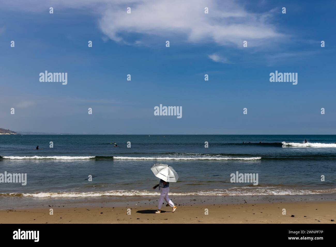Una donna si dirige verso Surfrider Beach a Malibu con un ombrello argentato. Foto Stock