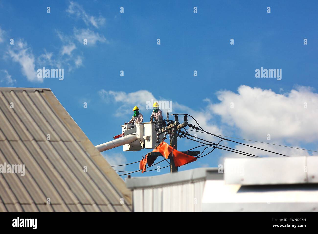 team di ingegneri elettrici che lavora sulla base di una piattaforma aerea o di cavi ad alta tensione collegati tramite gru sopra l'edificio contro il cielo blu Foto Stock