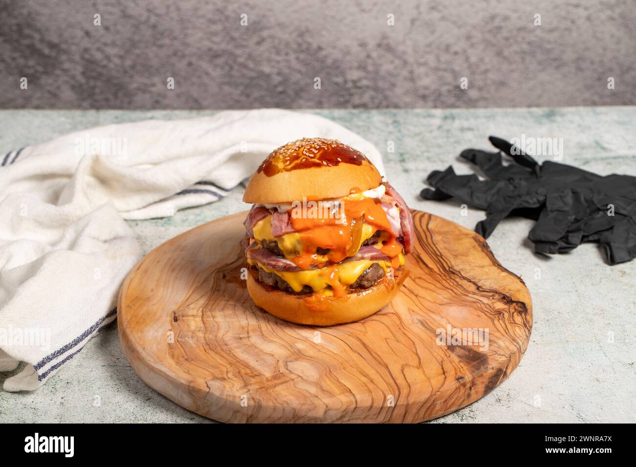 Doppio hamburger. Con formaggio Cheddar, cipolle caramellate, roast beef e salsa speciale. Hamburger con due polpette su tavola Foto Stock