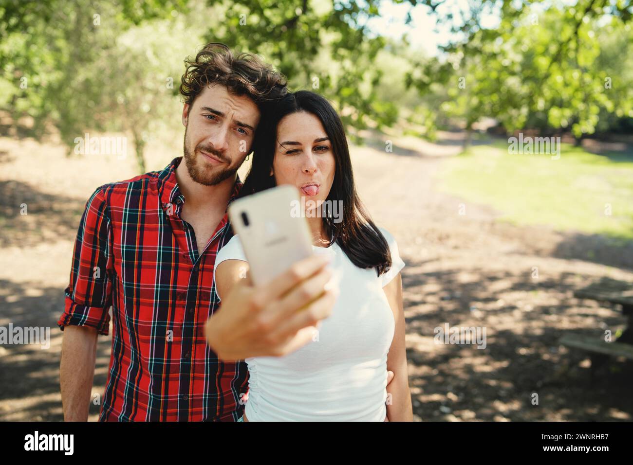 Una giovane coppia che si fa un divertente selfie con la lingua su un sentiero soleggiato - umore informale ma giocoso - catturando i ricordi in un ambiente naturale Foto Stock