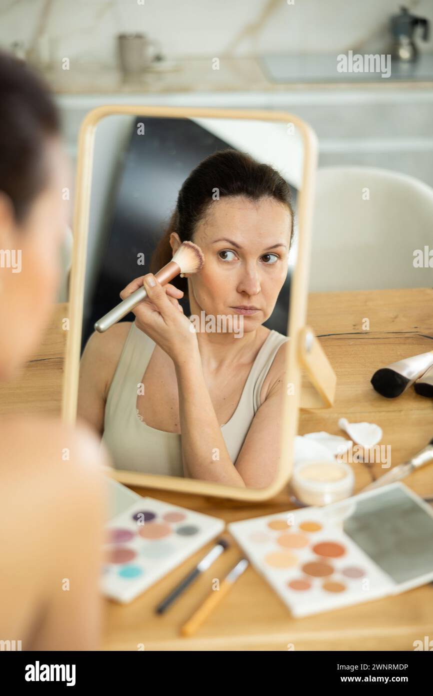 Donna di mezza età che applica il rossore sulle guance con un pennello per il trucco Foto Stock