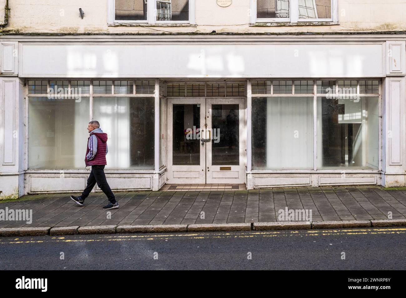 Un uomo che passa davanti a un negozio chiuso vuoto in Fore Street, nel centro di Bodmin, in Cornovaglia, nel Regno Unito. Foto Stock