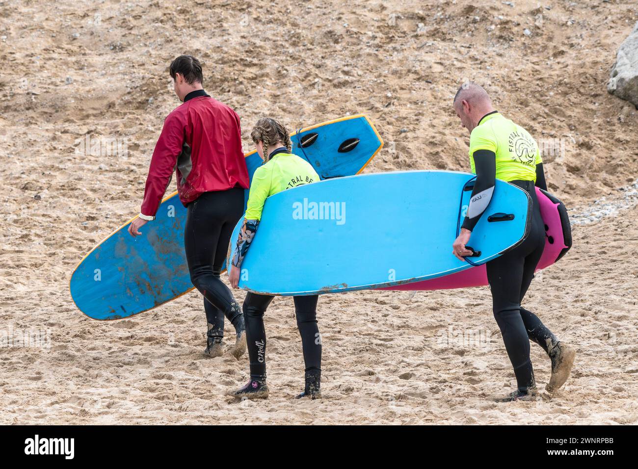 Un istruttore di surf e i suoi due studenti portano le loro tavole da surf a Fistral Beach a Newquay in Cornovaglia nel Regno Unito. Foto Stock