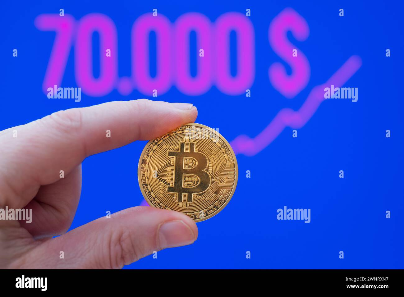 Bitcoin Coin between Fingers davanti a un prezzo di mercato di oltre 70.000 USD Foto Stock