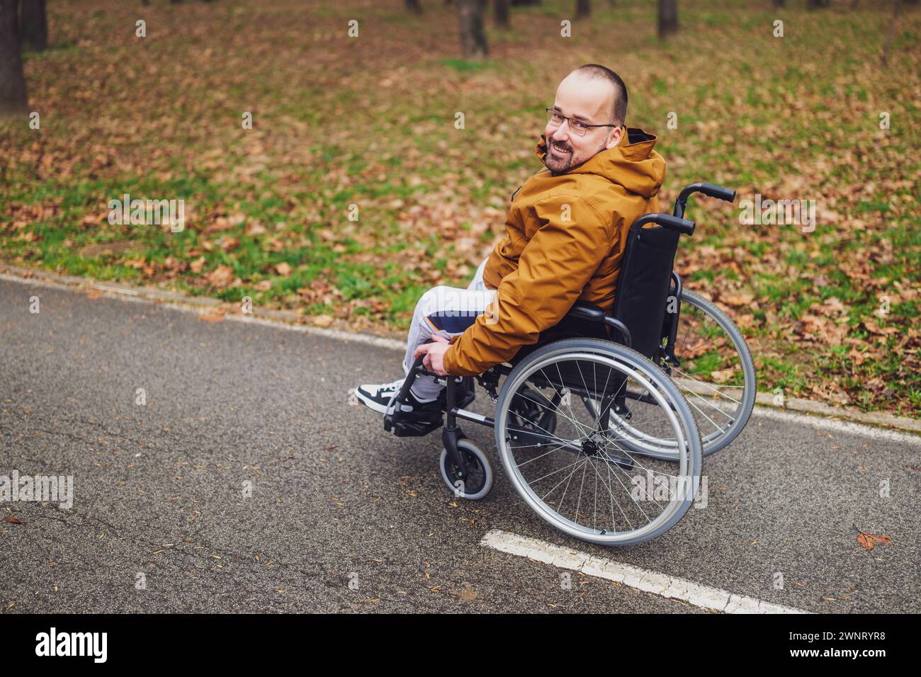 Ritratto di un uomo paraplegico in sedia a rotelle nel parco. Sta rotolando sulla strada. Foto Stock